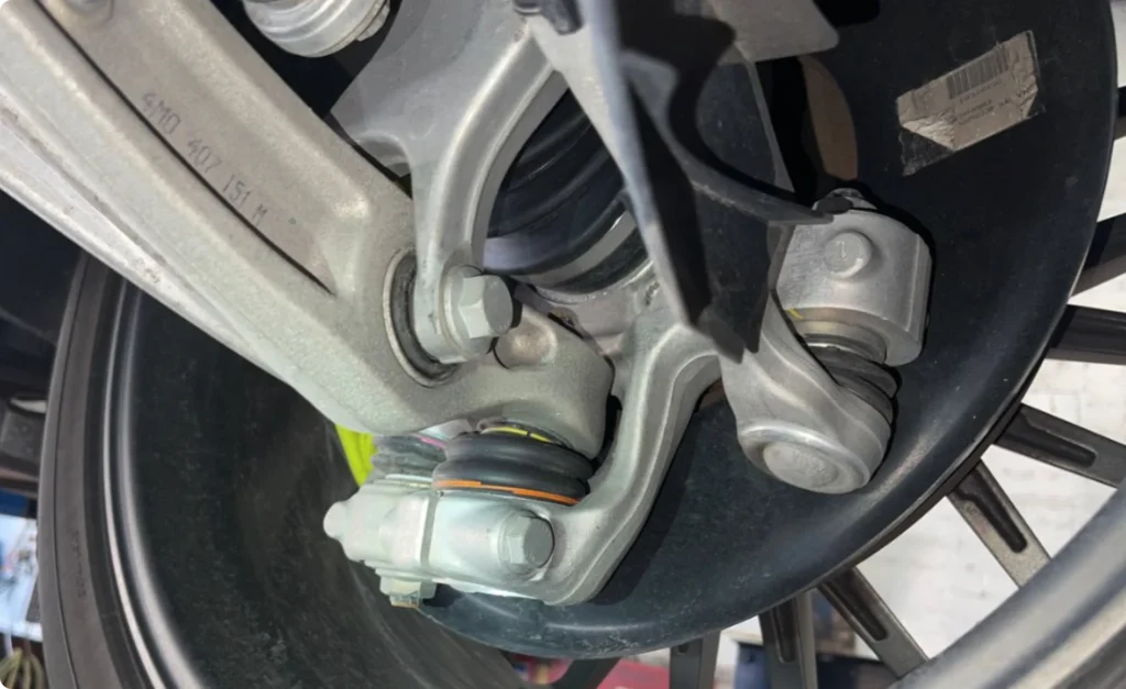 steering and suspension repair, auto repair in Poughkeepsie, NY at Foreign Car Specialists. Close-up of a car suspension system, showing metal parts including bolts, arms, and joints. The image focuses on the engineering and mechanical components under a vehicle, highlighting the silver-gray metal against a dark background.