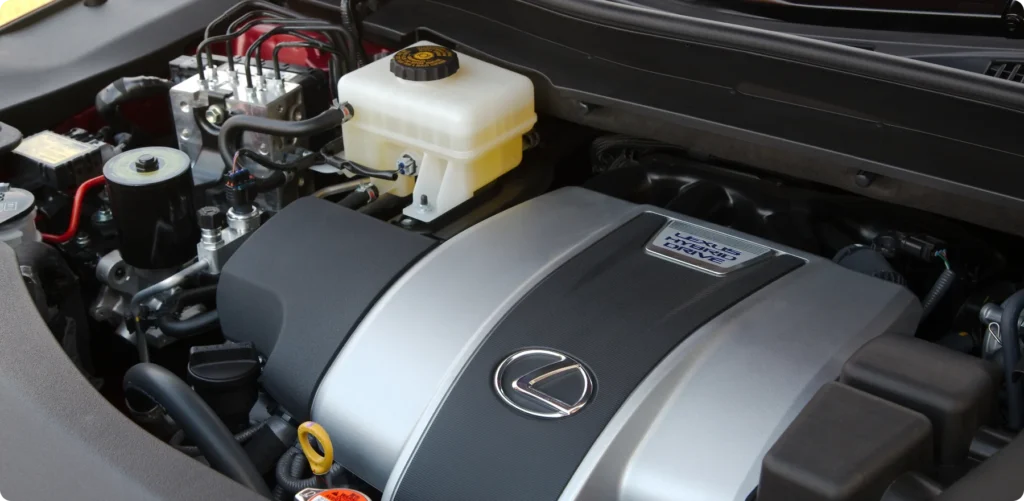 toyota lexus & scion repair, auto repair in Poughkeepsie, NY at Foreign Car Specialists. Close-up of a Lexus car engine, highlighting various components including a silver engine cover with the Lexus logo, fluid reservoirs, and connecting cables. The scene is under the hood with visible labels and connectors.